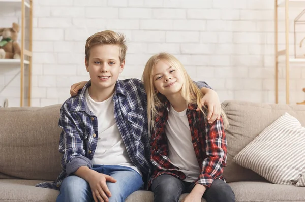 Bratr a sestra objímající usmívající se sedí na gauči doma — Stock fotografie