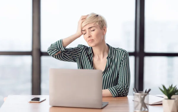 Signora toccando testa che soffre di dolore seduto in ufficio moderno — Foto Stock