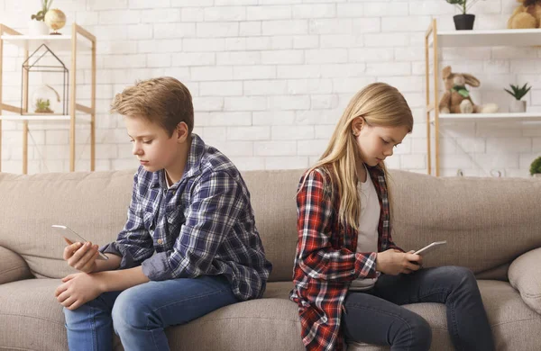 Брат и сестра используют телефоны, сидя дома на диване — стоковое фото