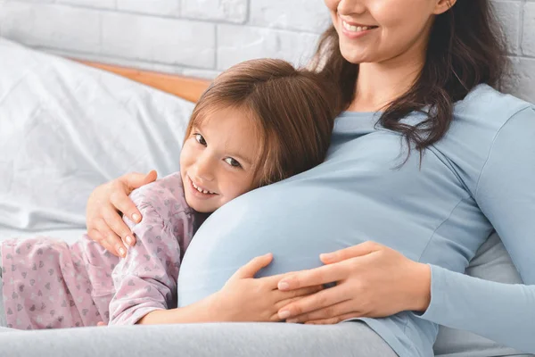 Primer plano de niña escuchando vientre de mamá embarazada —  Fotos de Stock