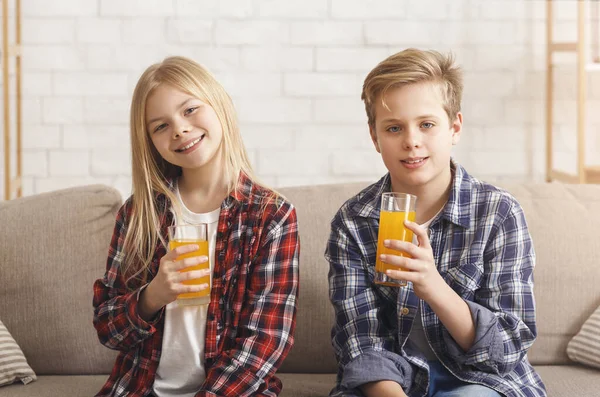 Брат и сестра пьют апельсиновый сок на диване в помещении — стоковое фото