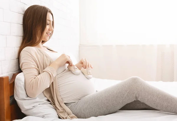 Boldog terhes nő játszik a hasával és apró csizmákkal — Stock Fotó