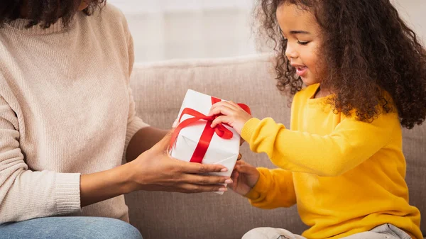Liten flicka mottar gåva från mor sitter på soffan inomhus — Stockfoto