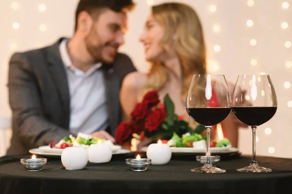 Casal afetuoso namoro no restaurante, copos com vinho tinto em primeiro plano — Fotografia de Stock