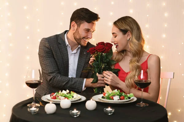 Bonito homem apresentando rosas para feliz namorada em data no restaurante — Fotografia de Stock