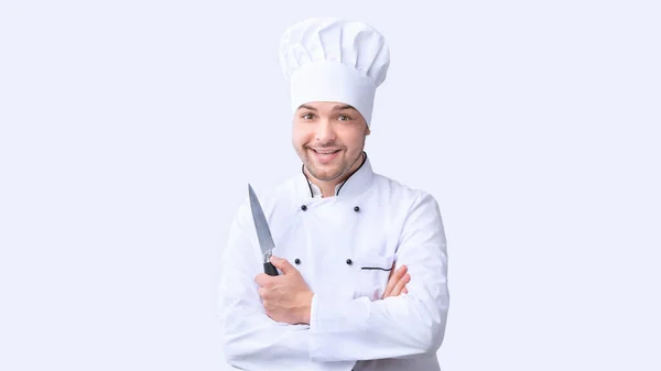 Cozinheiro positivo segurando faca de cozinha de pé, tiro estúdio — Fotografia de Stock