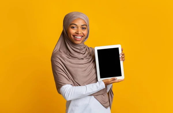 Chica afro alegre en pañuelo para la cabeza presentando tableta digital con pantalla negra —  Fotos de Stock