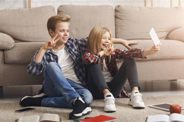 Brother And Sister Making Selfie Gesturing V-Sign Sitting On Floor