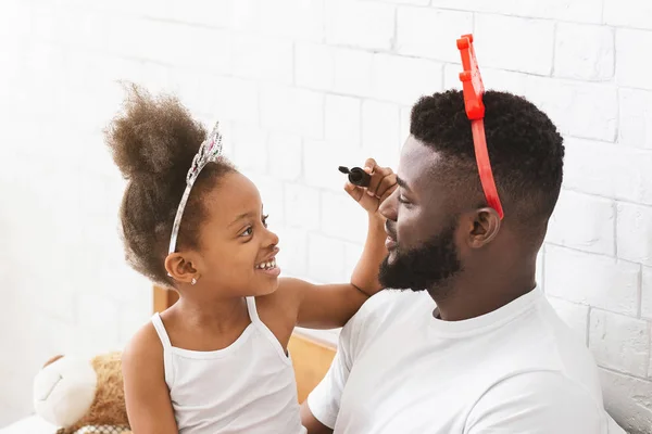 Klein zwart meisje zetten make-up op haar vader gezicht — Stockfoto