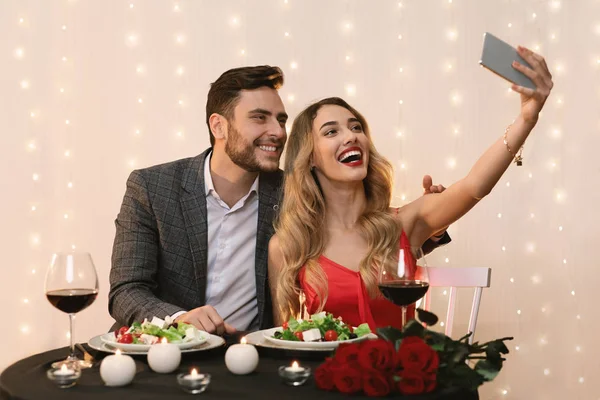 Романтическая пара, использующая смартфон, чтобы взять сальфи на свидание в ресторане — стоковое фото