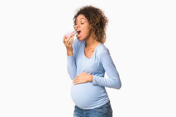 Pregnancy diet. Hungry afro expectant girl biting donut — Stok fotoğraf