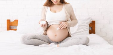 Pregnant woman moisturizing her belly with lotion, panorama
