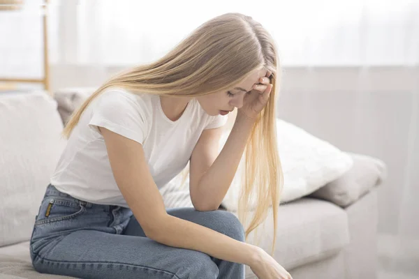 Depressed young girl sitting on couch at home alone — Stockfoto