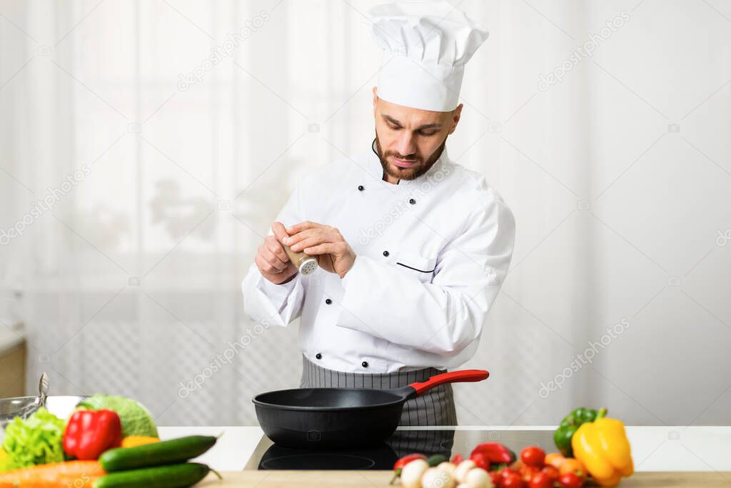 Chef Adding Pepper In Frying Pan Seasoning Dish In Kitchen