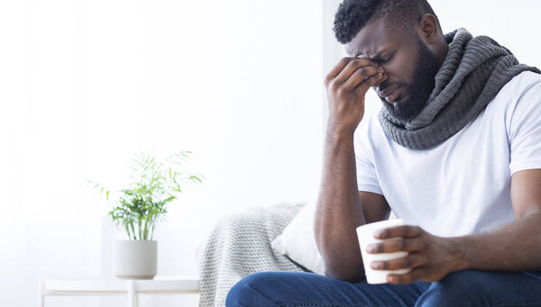 Black man with flu warming with cup with hot tea at home