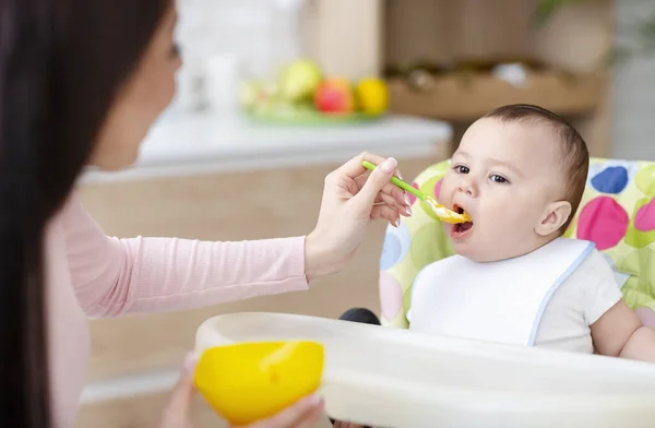 Mother feeding her baby son with porridge at kitchen — Stock Photo, Image