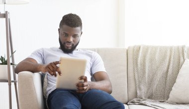 Dijital tablette haber okuyan konsantre Afrikalı adam