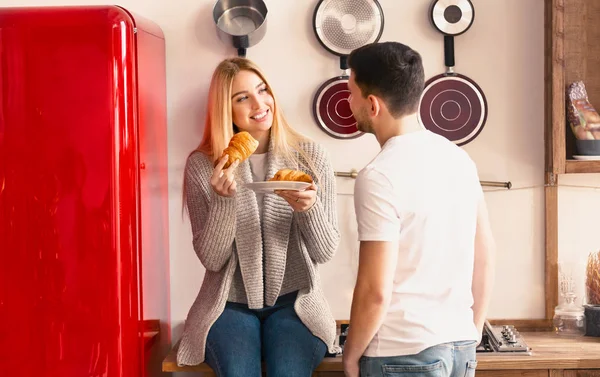 Genç çift mutfakta konuşuyor, kız kruvasan yiyor. — Stok fotoğraf