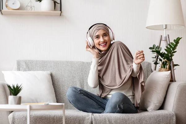Gadis Arab duduk di sofa dan mendengarkan musik dengan headphone nirkabel — Stok Foto