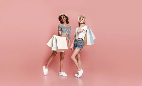 Две стильные девушки с мешками для покупок позируют на розовом фоне — стоковое фото