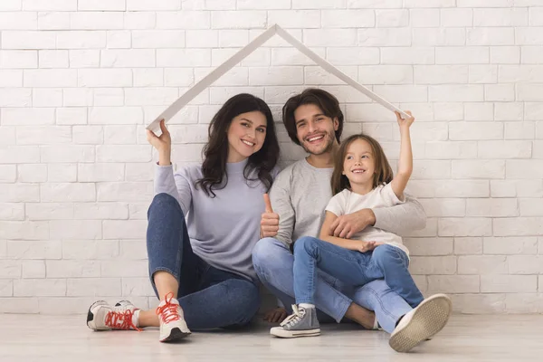 Happy Parents And Little Daughter Sitting On Floor Under Symbolic Roof — 스톡 사진