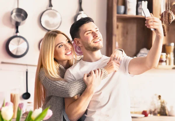 Alegre jovem casal fazendo selfie no celular na cozinha — Fotografia de Stock