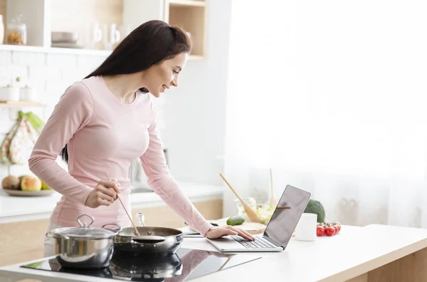 Jonge vrouw bereidt diner en browsen op laptop — Stockfoto