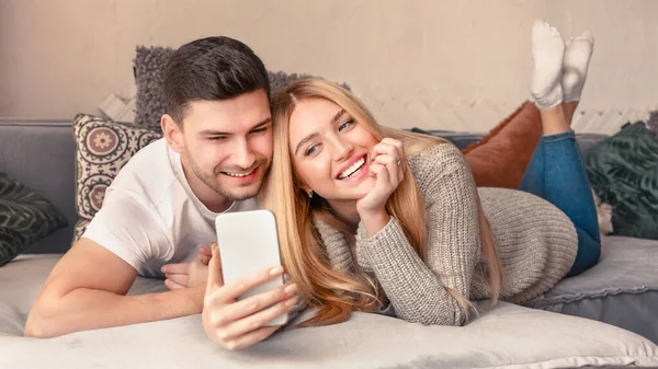 Счастливая пара лежит на кровати и делает селфи на мобильном телефоне — стоковое фото
