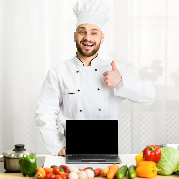 Szef kuchni Guy Holding Laptop Gesturing kciuki stojące w kuchni — Zdjęcie stockowe