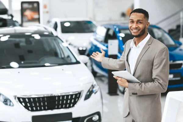 Afro vendedor mostrando nuevo auto de pie en salón de exhibición de concesionarios de automóviles —  Fotos de Stock
