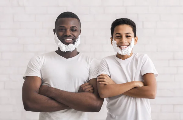 Preto pai e sol posando com barba de espuma e braços dobrados — Fotografia de Stock