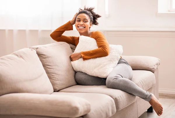 ゆったりとしたアフリカの女性は、カウチの大きな枕の屋内に座って — ストック写真