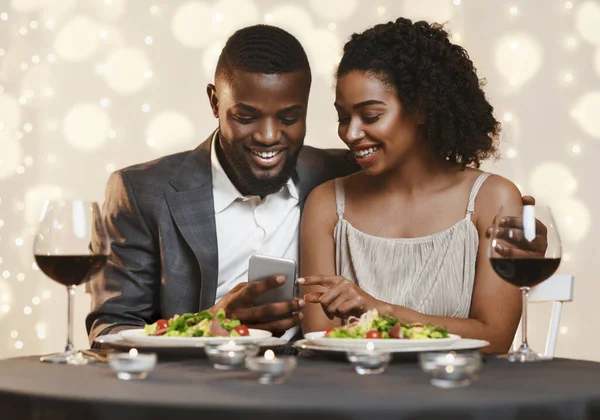 Νεαρό μαύρο ζευγάρι βλέποντας φωτογραφίες στο smartphone, εστιατόριο εσωτερικό — Φωτογραφία Αρχείου
