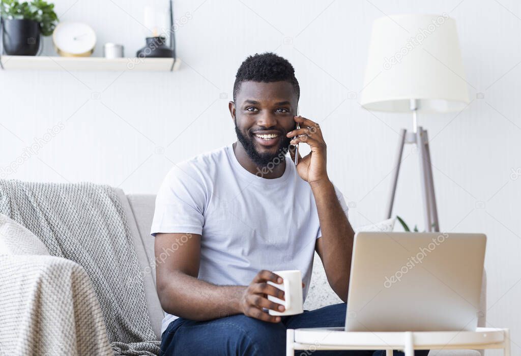 Positive african guy working on laptop and calling on phone
