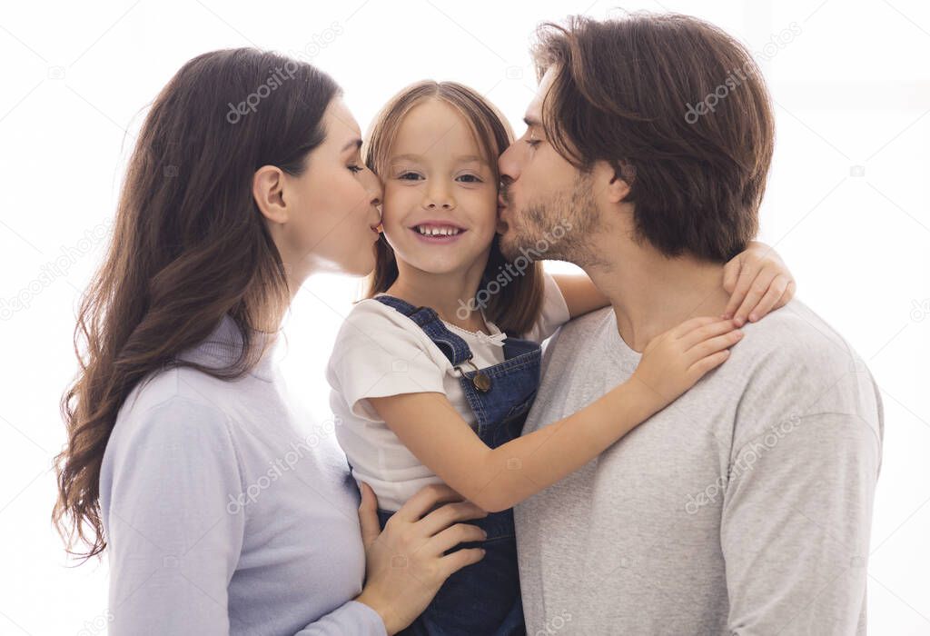 Portrait Of Happy Young Parents Kissing Cheeks Of Their Little Daughter