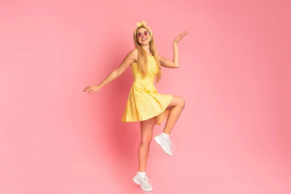 Wesoła kobieta tańczy przeskakując przez różową ścianę studia — Zdjęcie stockowe