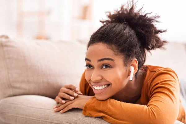 Улыбающаяся афроамериканская девочка слушает музыку, расслабляясь дома — стоковое фото
