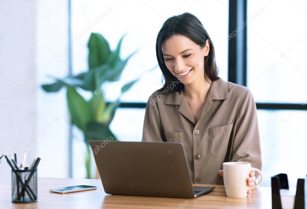 Portrait of smiling woman working on laptop with tea