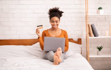 Çevrimiçi alışveriş yapan Afro Kadın Evde Yatakta Oturuyor