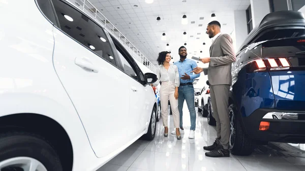 Afro Salesman Selling Car To Customers Standing In Dealership Showroom — Stock Photo, Image