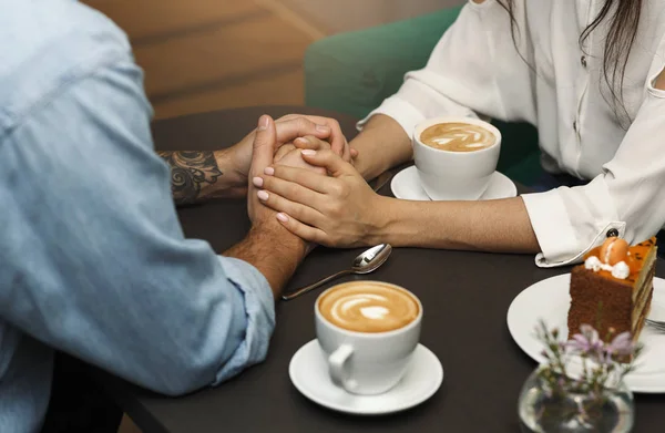 Nierozpoznawalna para trzymająca się za ręce, pijąca kawę w kawiarni, przycięta — Zdjęcie stockowe