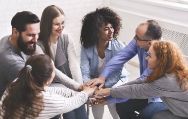 Bir grup mutlu insan terapi seansında el ele tutuşuyor.
