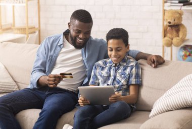 Neşeli Siyah Baba dijital tablet kullanarak oğluyla internetten alışveriş yapıyor.