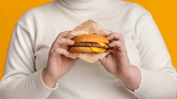 Nierozpoznawalna kobieta pokazuje hamburgera wołowego przed kamerą, uzależniona od fast foodów — Zdjęcie stockowe