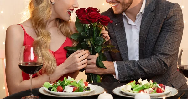Nerozpoznatelný muž dává růže kytice na přítelkyni na rande v restauraci — Stock fotografie
