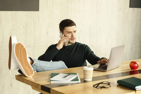 Ελεύθερος επαγγελματίας μιλώντας στο τηλέφωνο κάθεται με τα πόδια στο γραφείο εσωτερική — Φωτογραφία Αρχείου