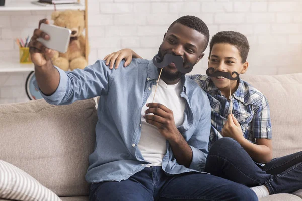Joyful black father and son posing for selfie at home
