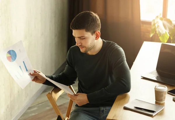 Millennial Guy κοιτάζοντας μέσα από τα έγγραφα εργασίας που κάθεται στο χώρο εργασίας — Φωτογραφία Αρχείου