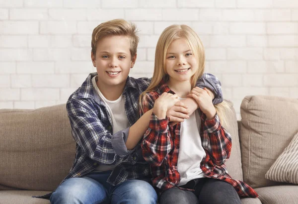 Милый мальчик и девушка обнимаются, сидя дома на диване — стоковое фото