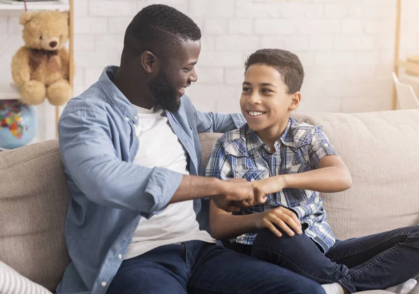 Pai e filho batendo punhos sentados no sofá em casa — Fotografia de Stock